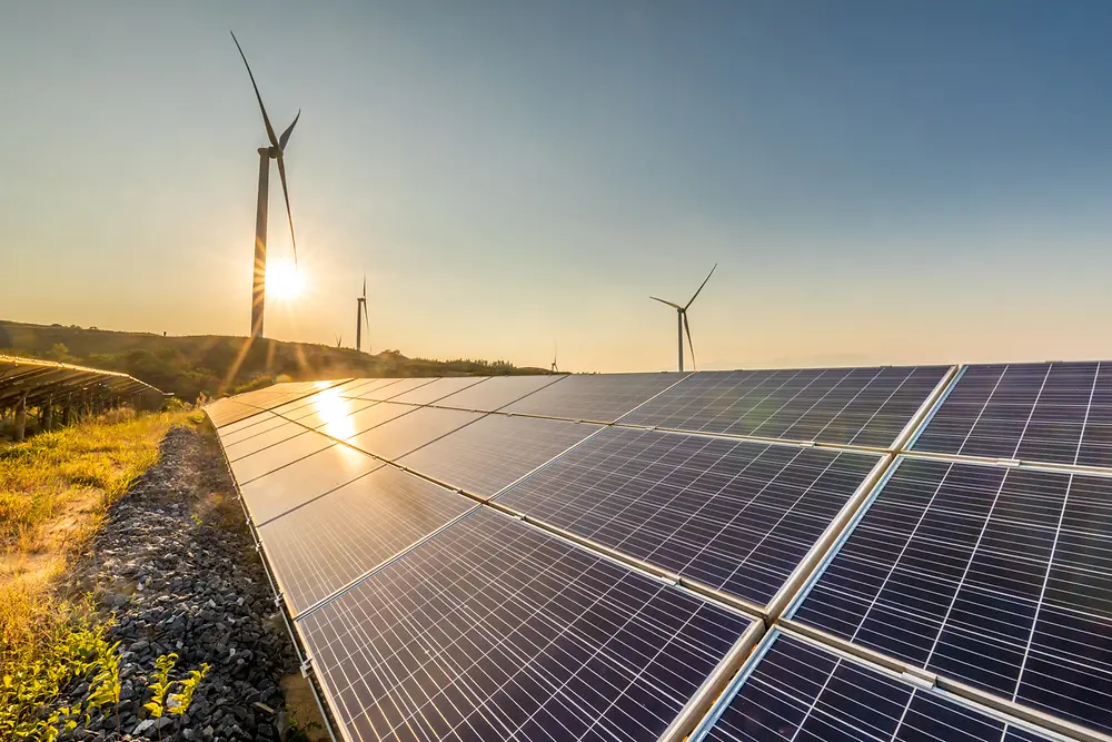 Paneles solares al atardecer con molinos de viento en el fondo