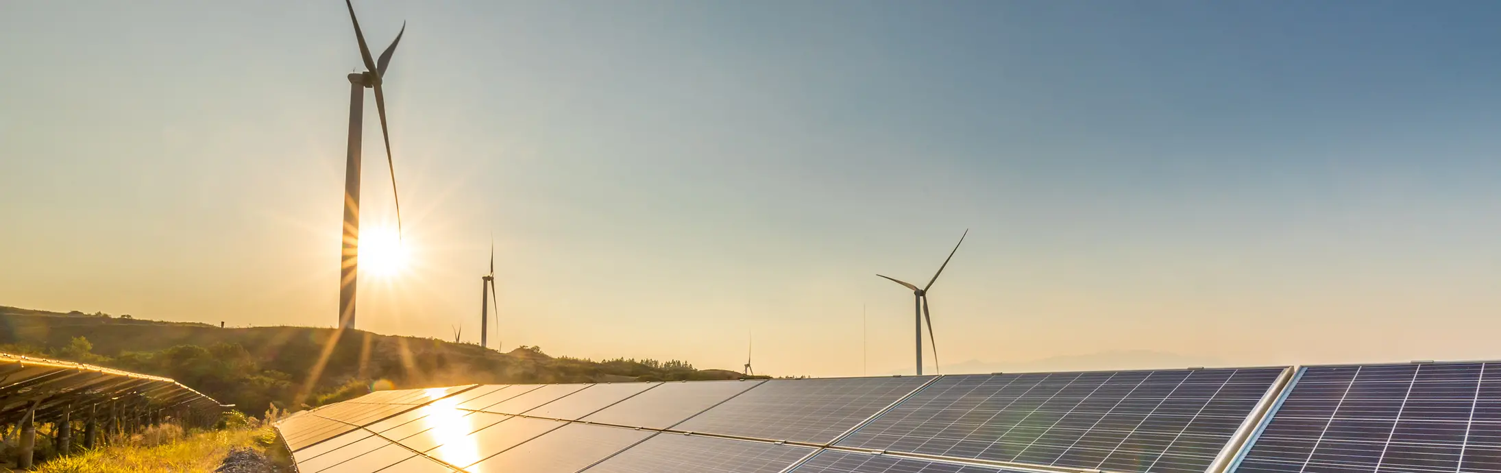 Paneles solares al atardecer con molinos de viento en el fondo